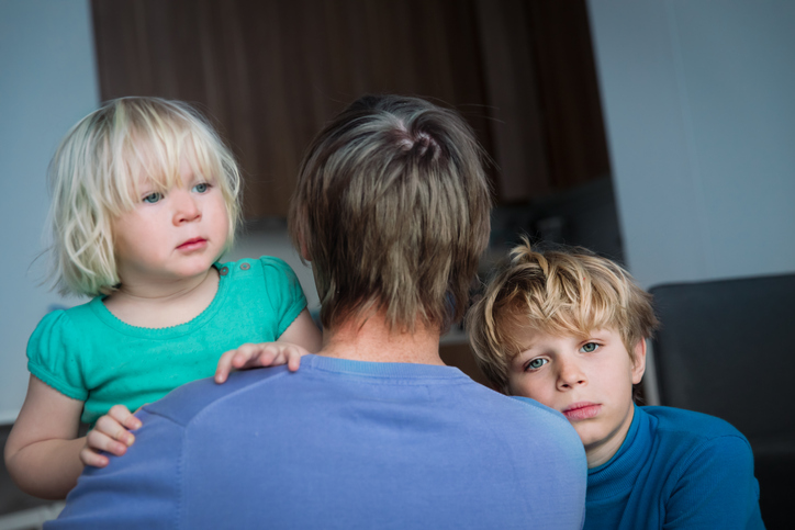 Two upset children leaning on their father looking for comfort